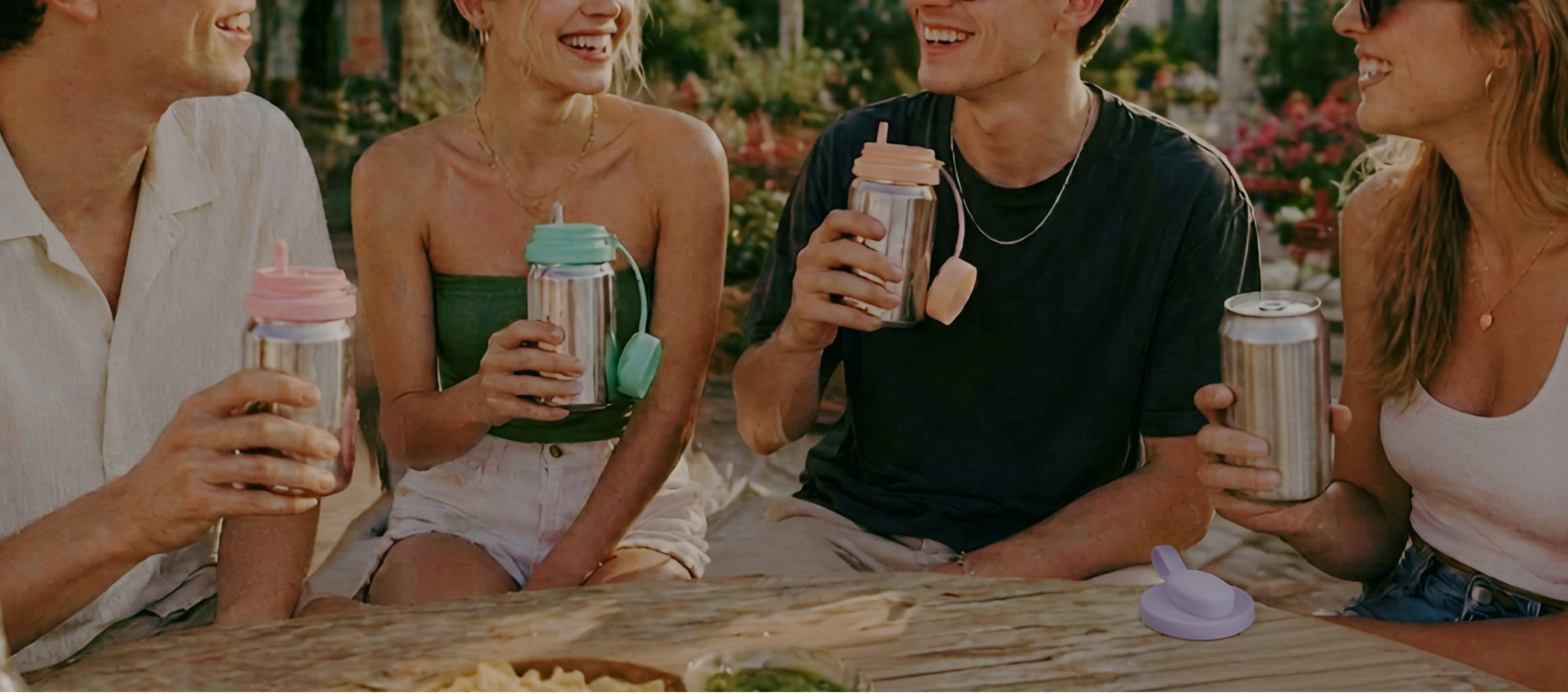 Four friends sitting together outdoors, holding drinks with straws.